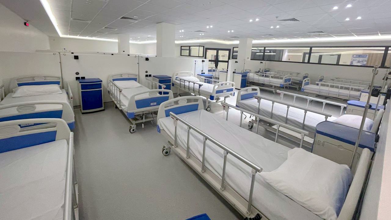 The NAMA Bio-Center participant ward: rows of blue-and-white clinical beds in open, partitioned bays under bright ceiling lighting.