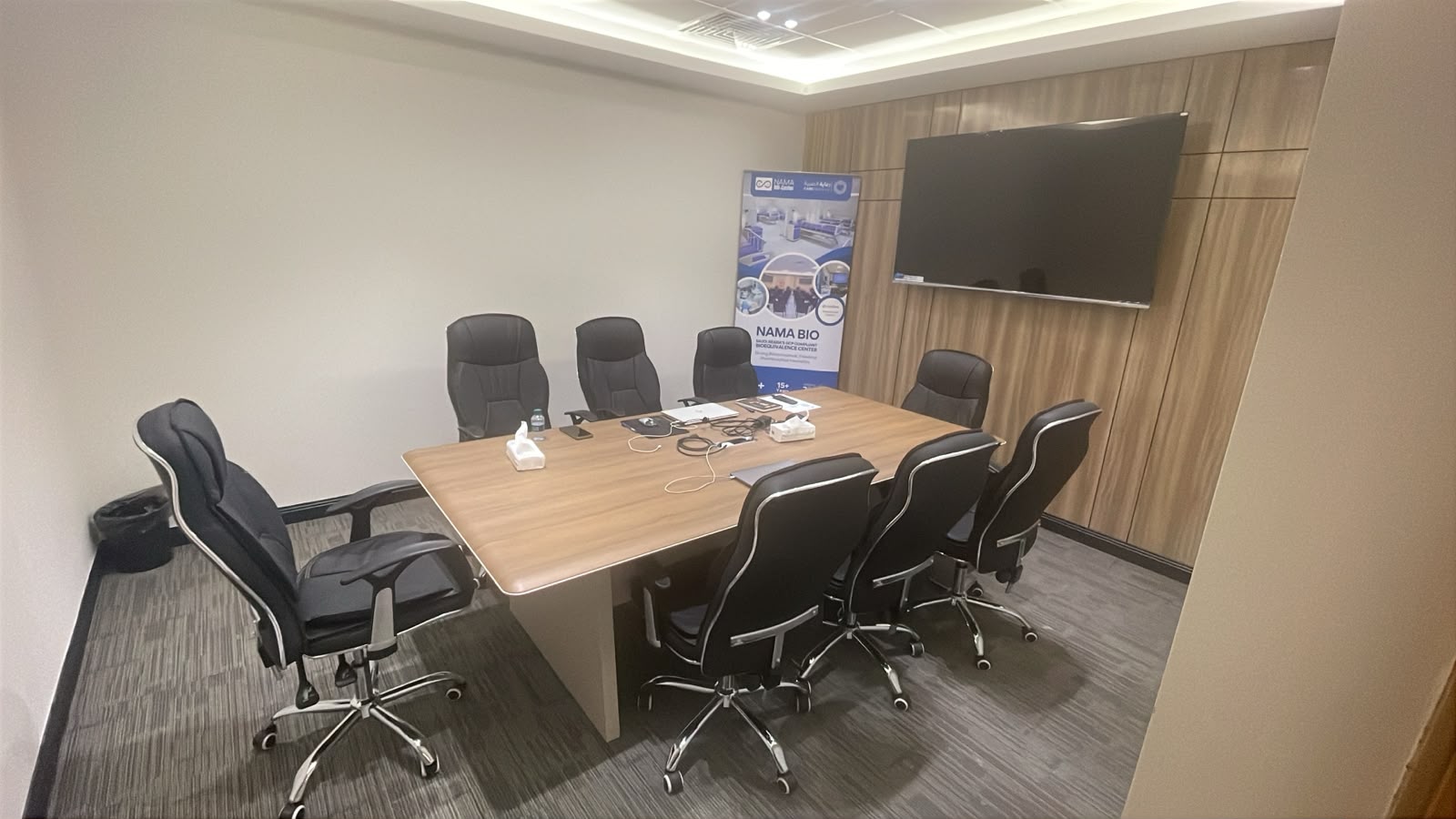 The board room at NAMA Bio-Center, with an eight-seat wooden meeting table, high-backed chairs and a large wall-mounted screen on wood panelling.