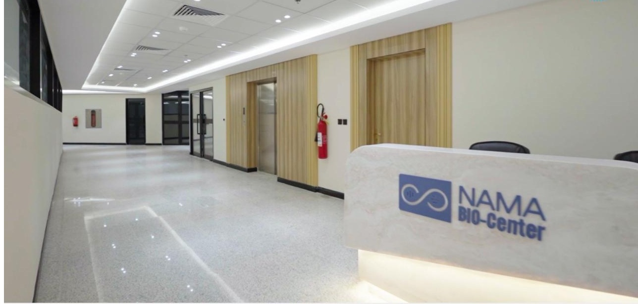 The NAMA Bio-Center reception desk, a pale stone counter carrying the blue NAMA BIO-Center logo, facing a bright terrazzo corridor.